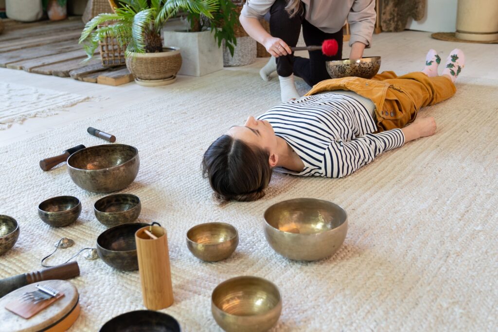 Recovery massage with tibetan singing bowls. Female at asian sound therapy with bronze bowls gong